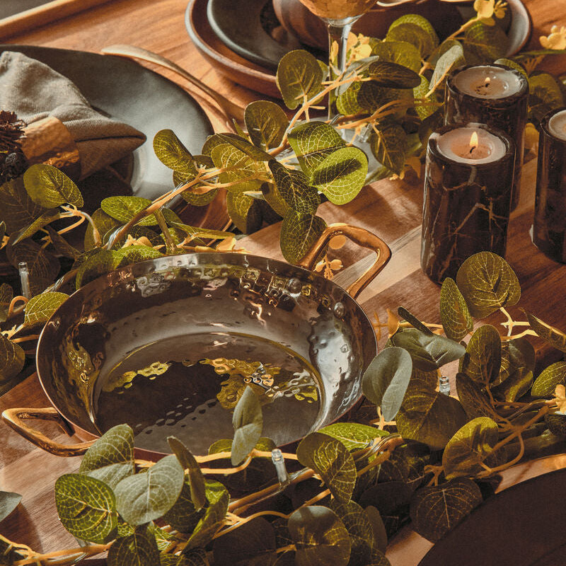 Dining table setting with wine glasses, plates, and greenery on a wooden surface.