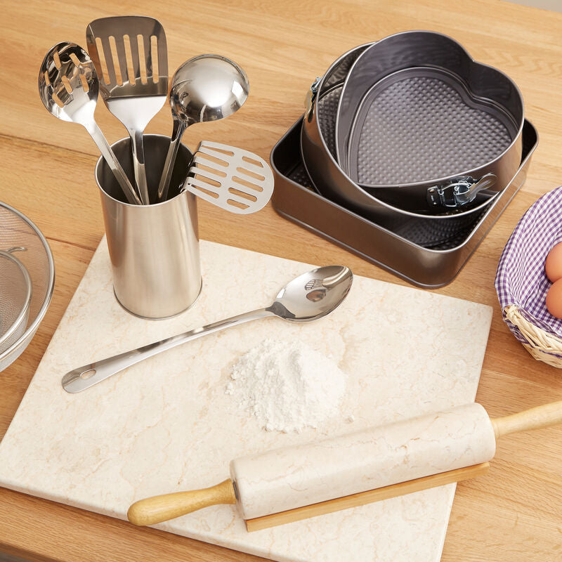 Kitchen utensils and tools on a wooden table including a rolling pin, measuring cups, and a basket of eggs.