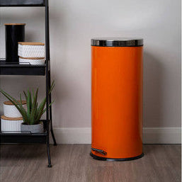 Orange trash can next to a black metal shelf with jars and a plant on a gray wall background