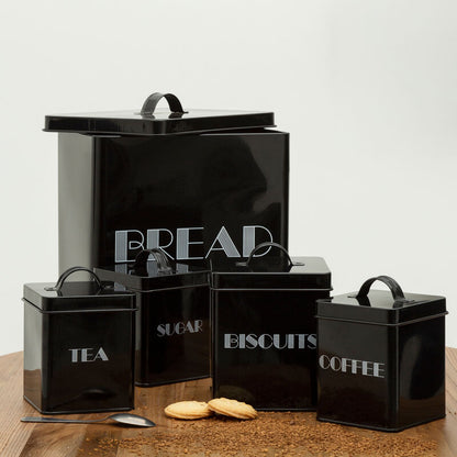 Set of black kitchen canisters with labels on a wooden surface