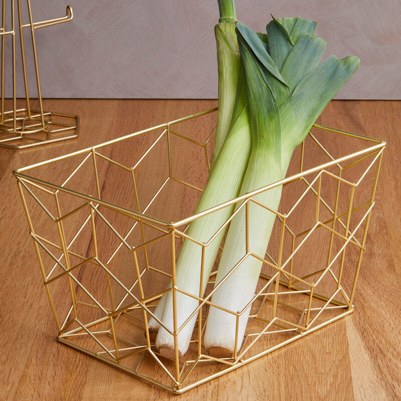 Gold geometric wire basket with leeks on a wooden surface