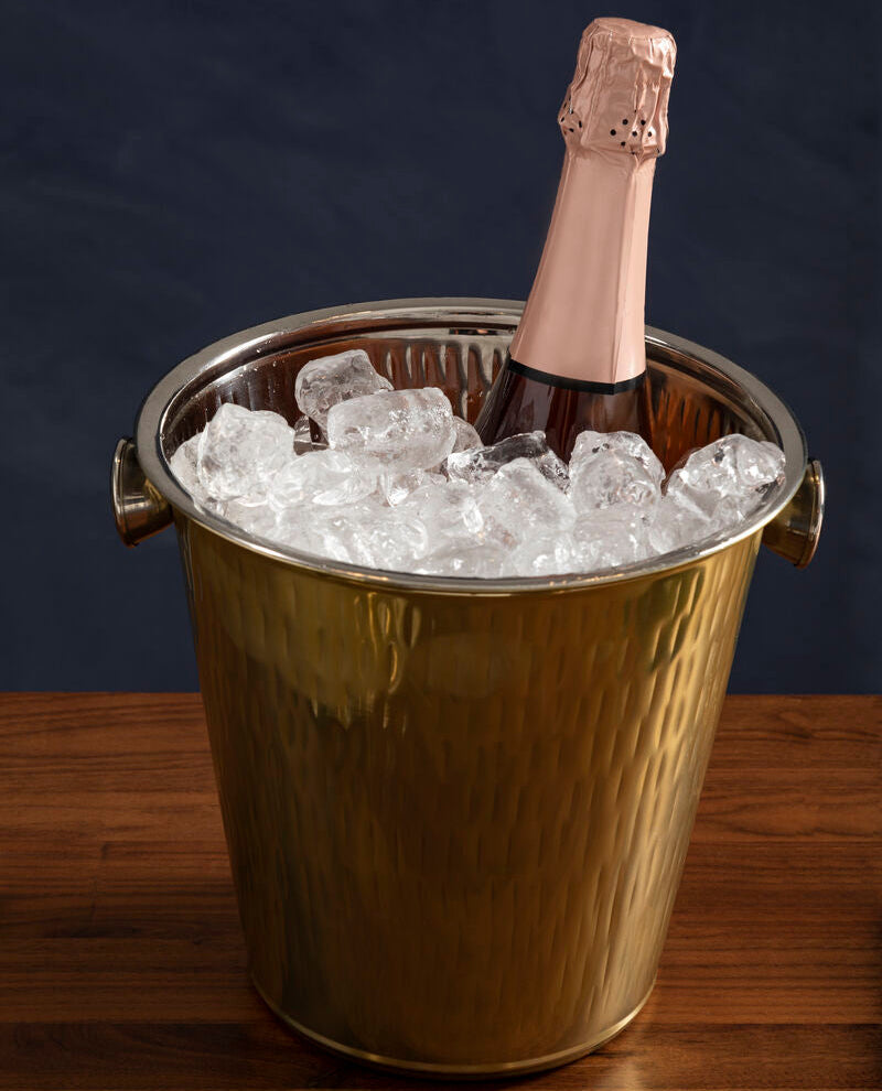 Bottle of champagne in a gold ice bucket on a wooden surface with a dark background
