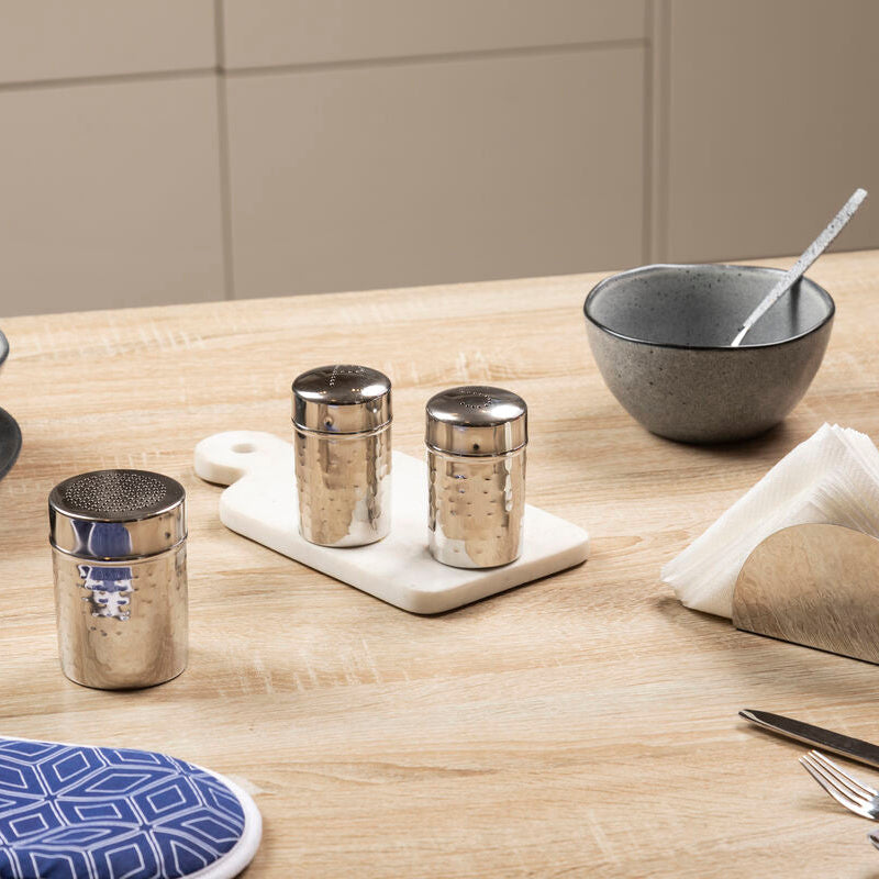 Kitchen setting with gray bowls, silver tumblers, and a cutting board on a wooden table.