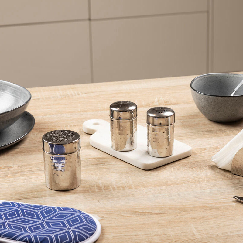 Kitchen setting with gray bowls, silver tumblers, and a cutting board on a wooden table.