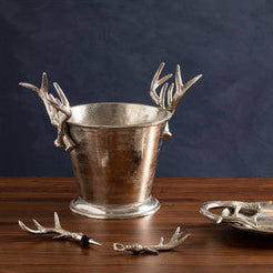 Decorative metal container with antler design on a wooden surface against a dark background