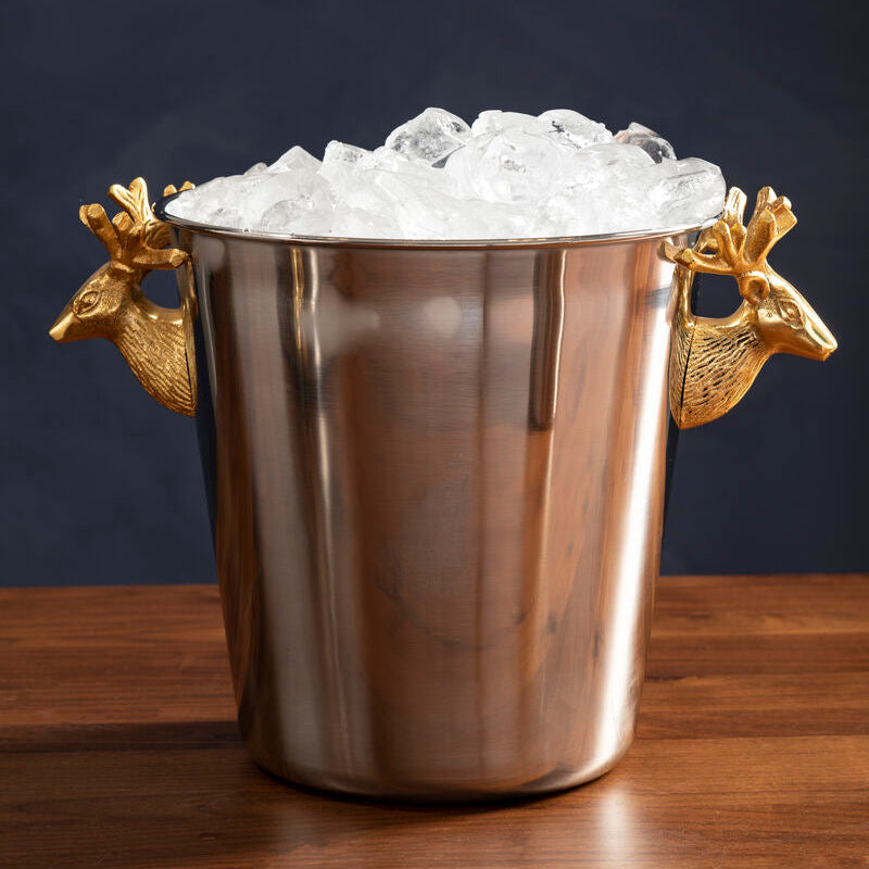 Silver ice bucket with gold handles filled with ice on a wooden surface.