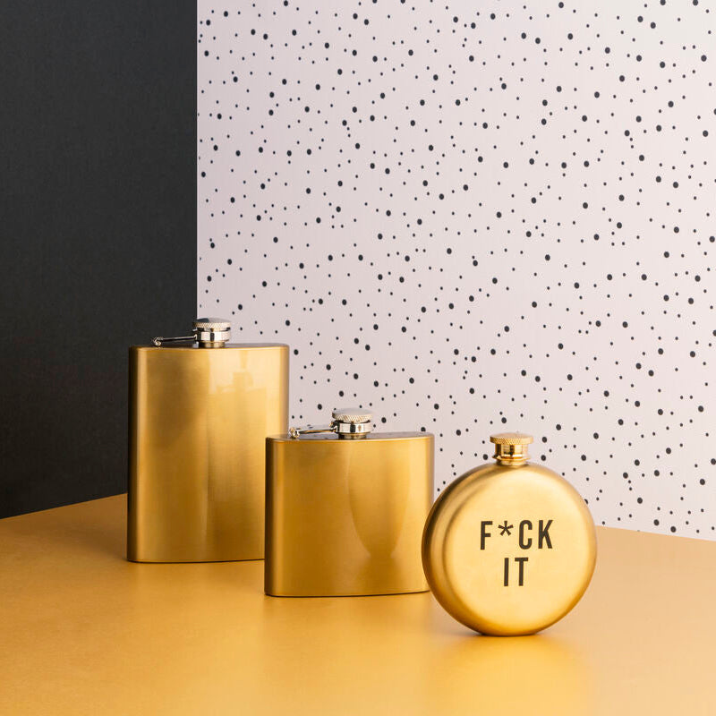 Three gold flasks on a yellow surface with a polka dot wall in the background