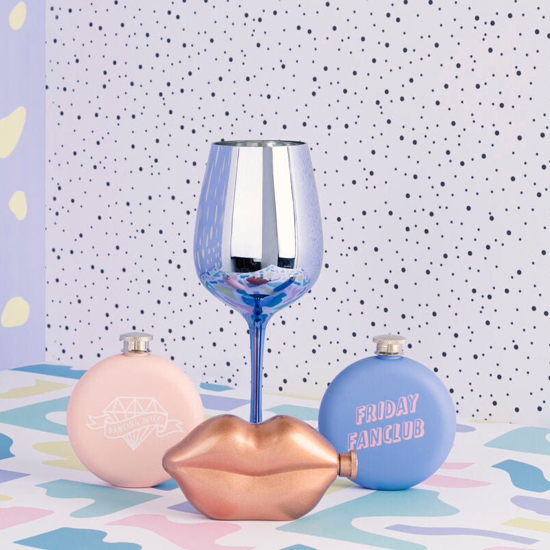 Decorative lip-shaped bottles and a wine glass on a patterned surface with a polka dot wall background.