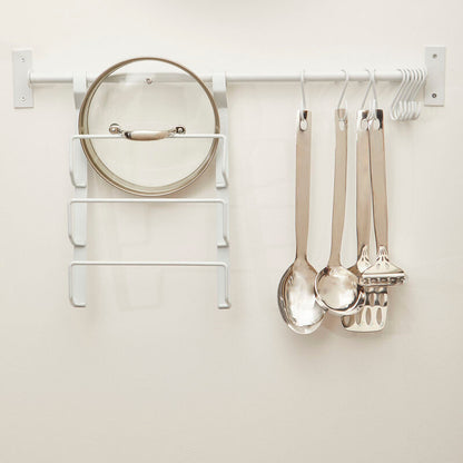 Wall-mounted clock and utensil holder with kitchen tools on a white wall