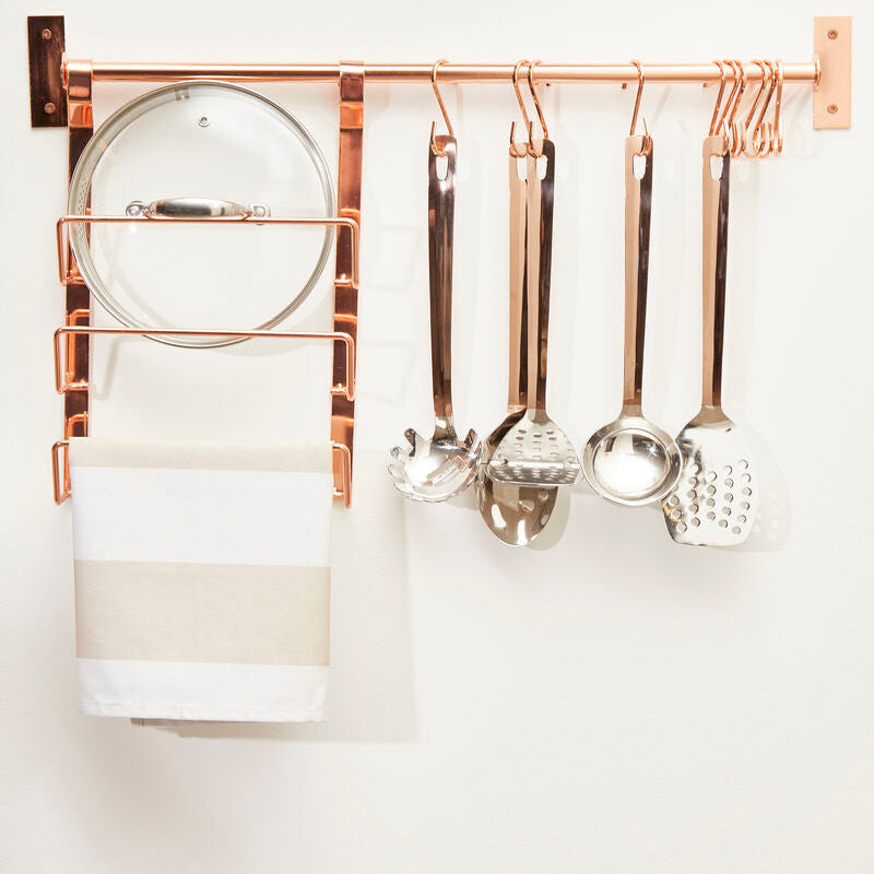 Wall-mounted kitchen utensil holder with copper accents on a white wall.