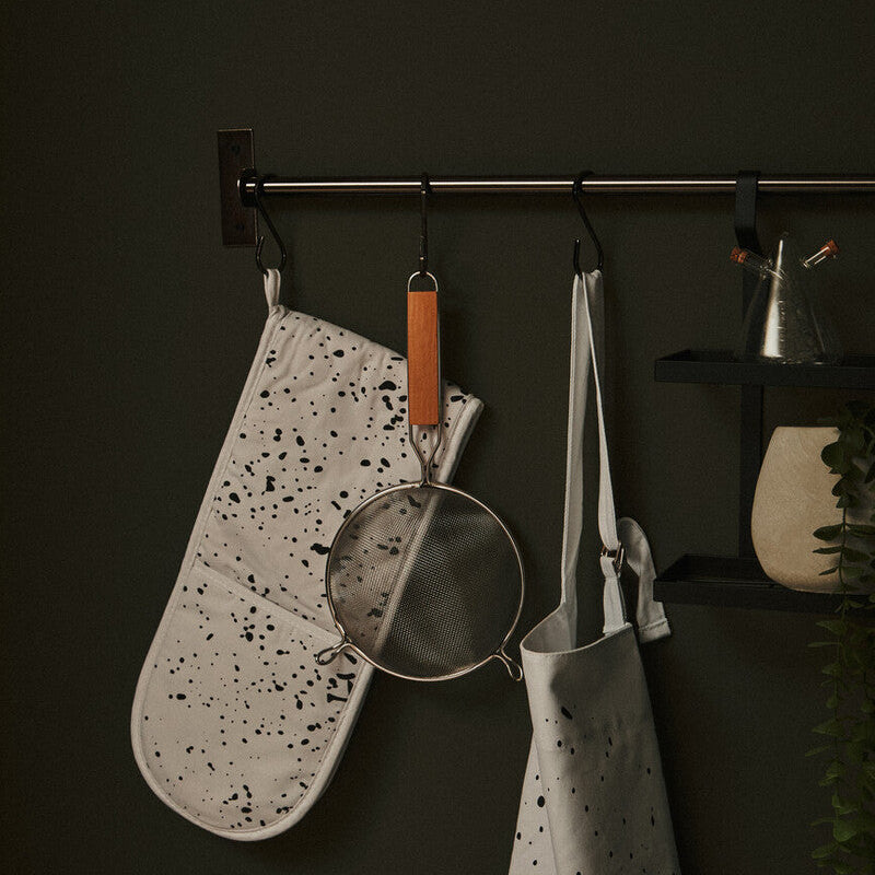 Speckled apron, pot holder, and strainer hanging on a dark wall.