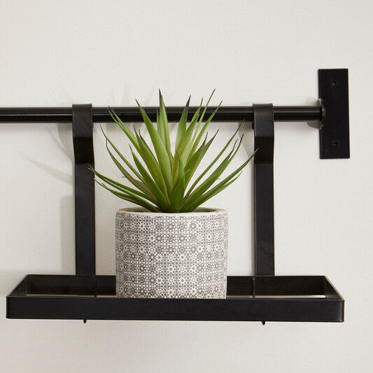 Black metal wall shelf with a potted plant on a white background