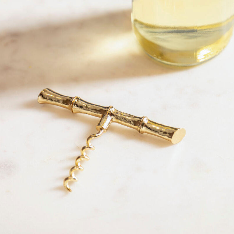 Gold corkscrew on a light surface with a glass of white wine in the background