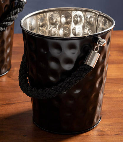 Black metal ice bucket with textured surface and handle on a wooden surface