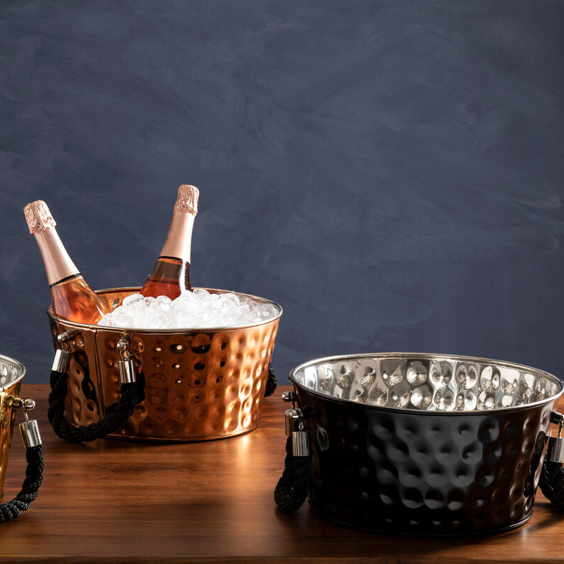 Three metallic ice buckets with champagne bottles on a wooden surface against a dark background