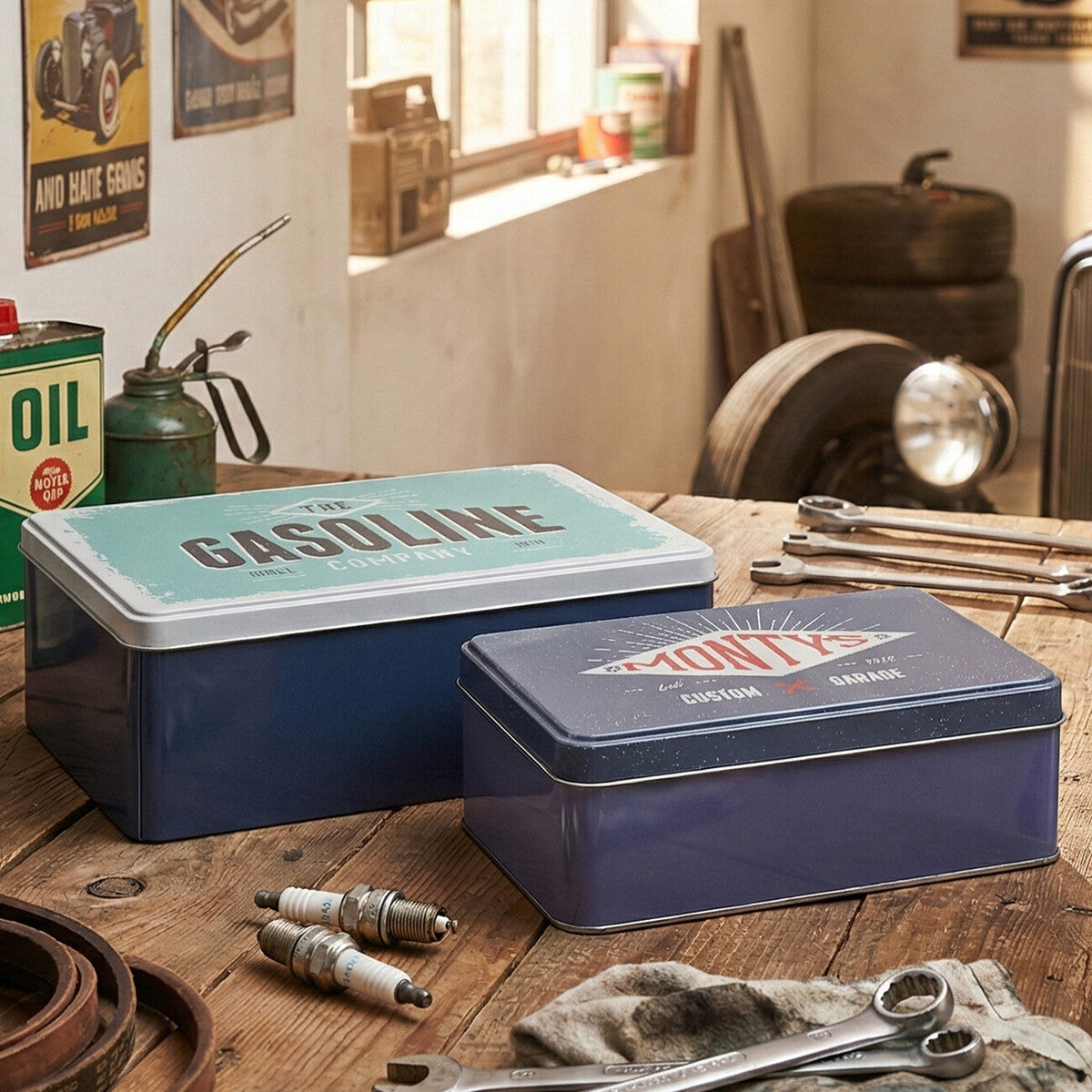 Two vintage-style metal storage boxes on a wooden table with tools and oil cans in a garage setting.