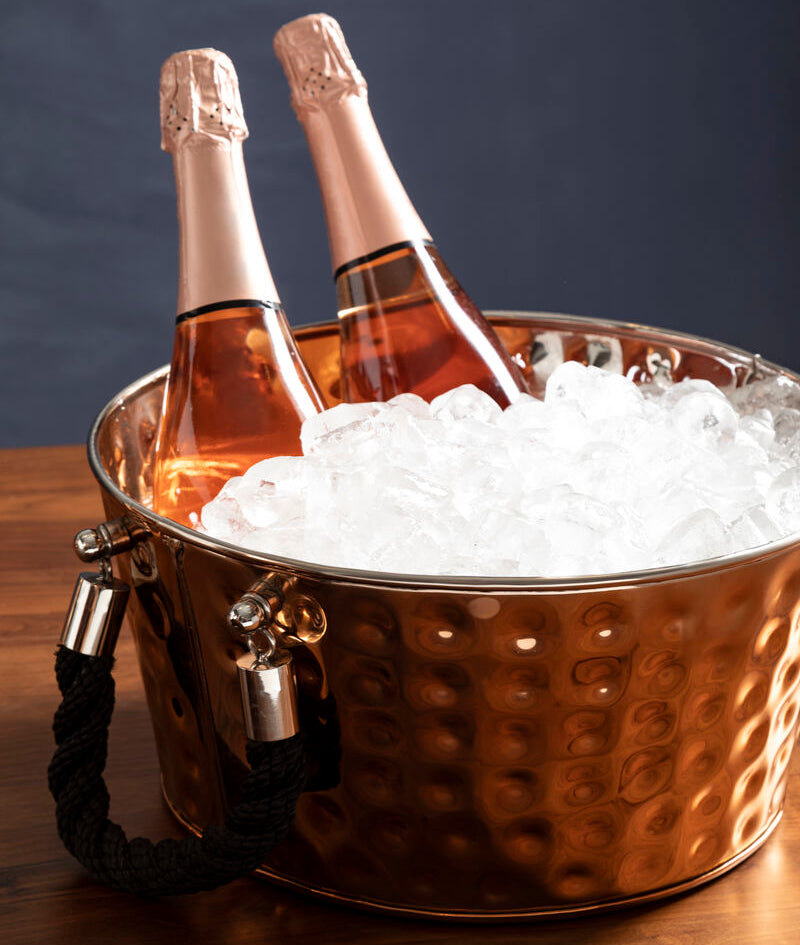 Two bottles of champagne in a copper ice bucket on a wooden surface with a dark background
