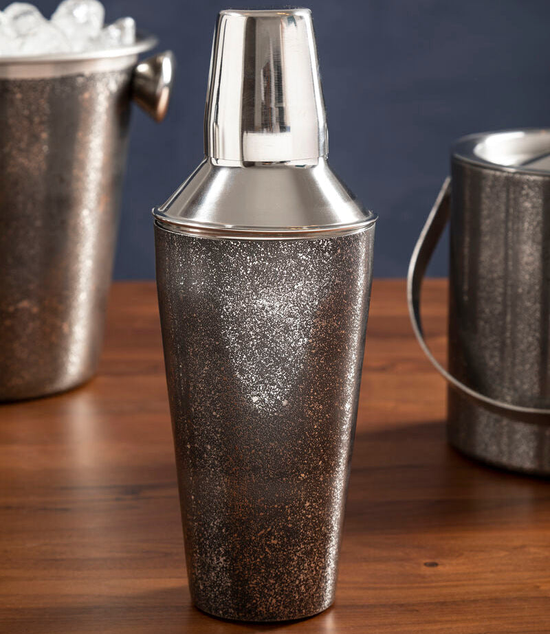 Silver cocktail shaker on a wooden surface with ice buckets in the background.