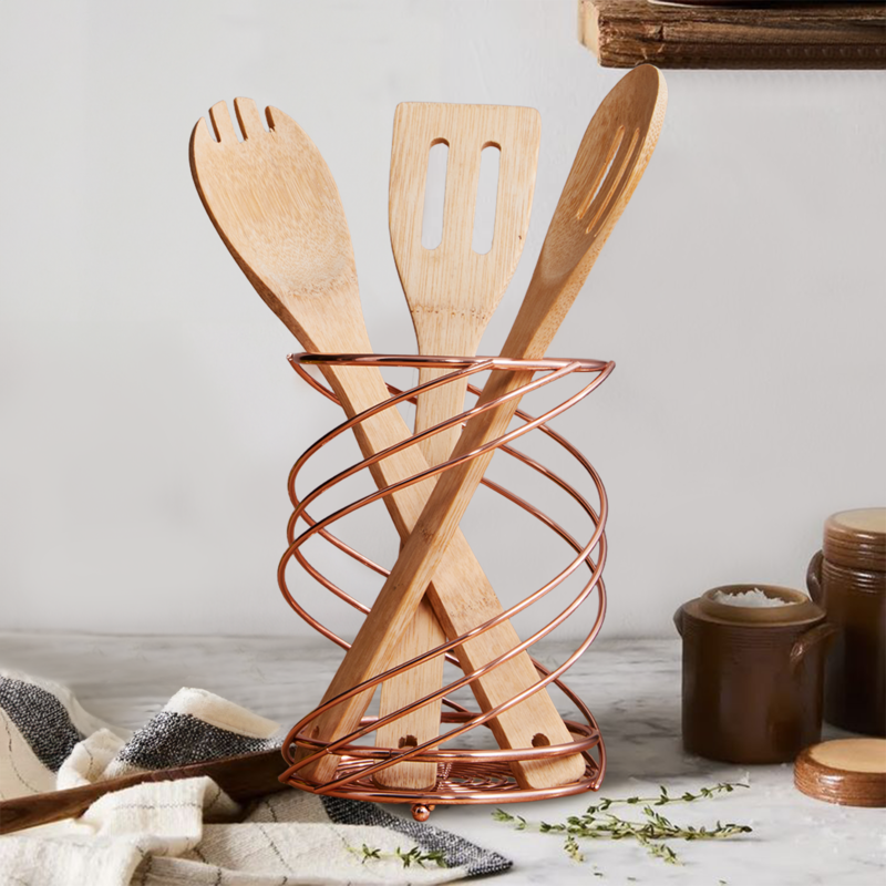 Wooden utensils in a copper holder on a kitchen counter.