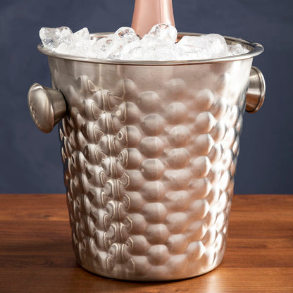 Bottle of champagne in a textured silver ice bucket on a wooden surface with a dark background