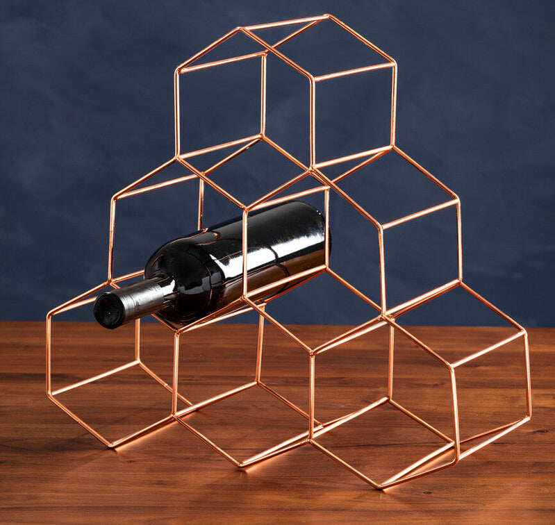 Geometric copper wine bottle holder on a wooden surface with a dark blue background