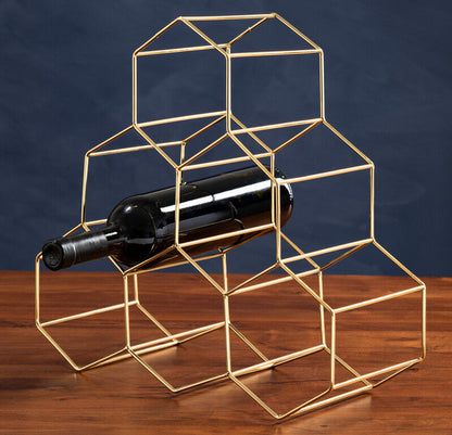 Gold geometric wine bottle holder with a wine bottle on a wooden surface and dark blue background