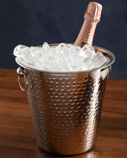 Silver ice bucket with ice and a bottle of champagne on a wooden surface.