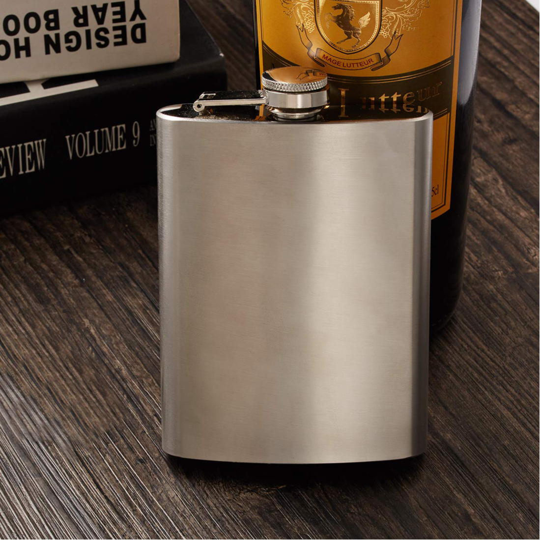 Metallic flask on a wooden surface with a bottle in the background