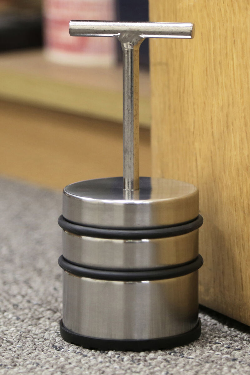Metallic door stopper with a T-shaped handle on a carpeted floor.