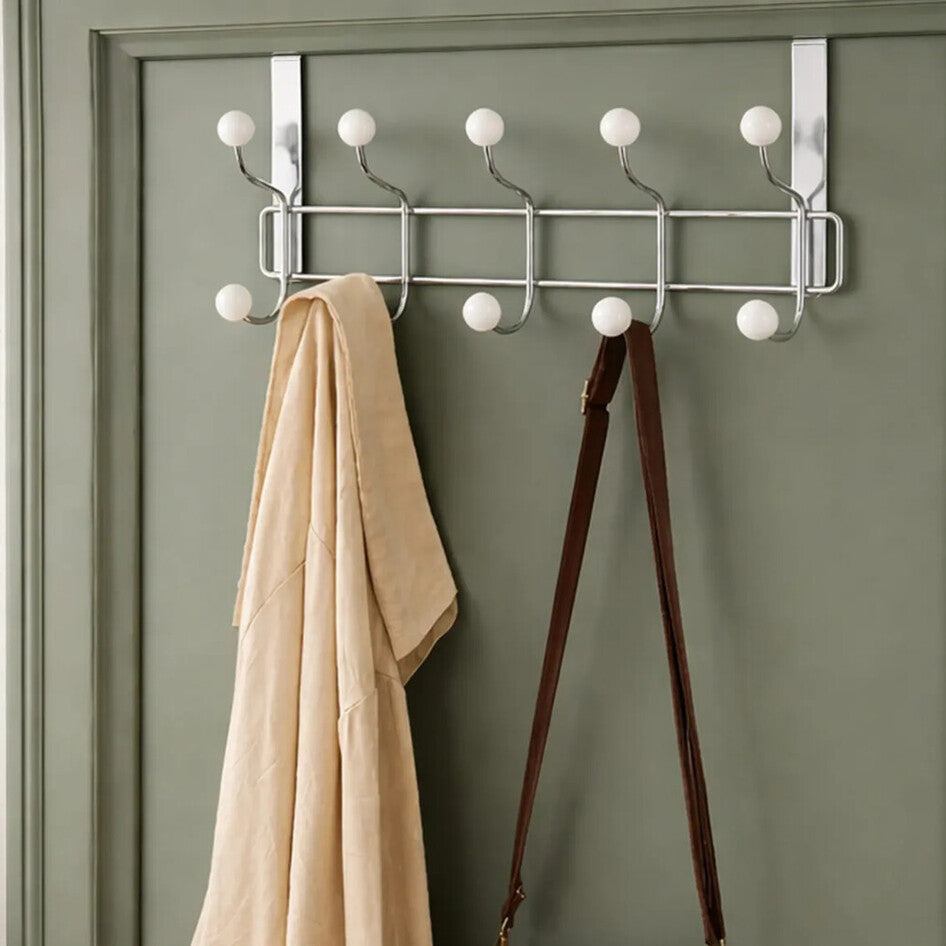 Metal coat rack with hooks on a green door, holding a beige coat and brown bag, with &