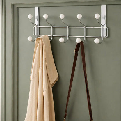Metal coat rack with hooks on a green door, holding a beige coat and brown bag, with &