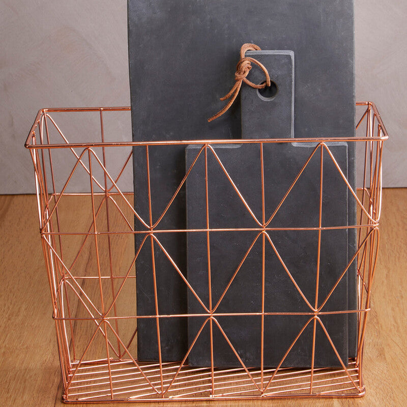 Copper wire basket with a gray cutting board on a wooden surface