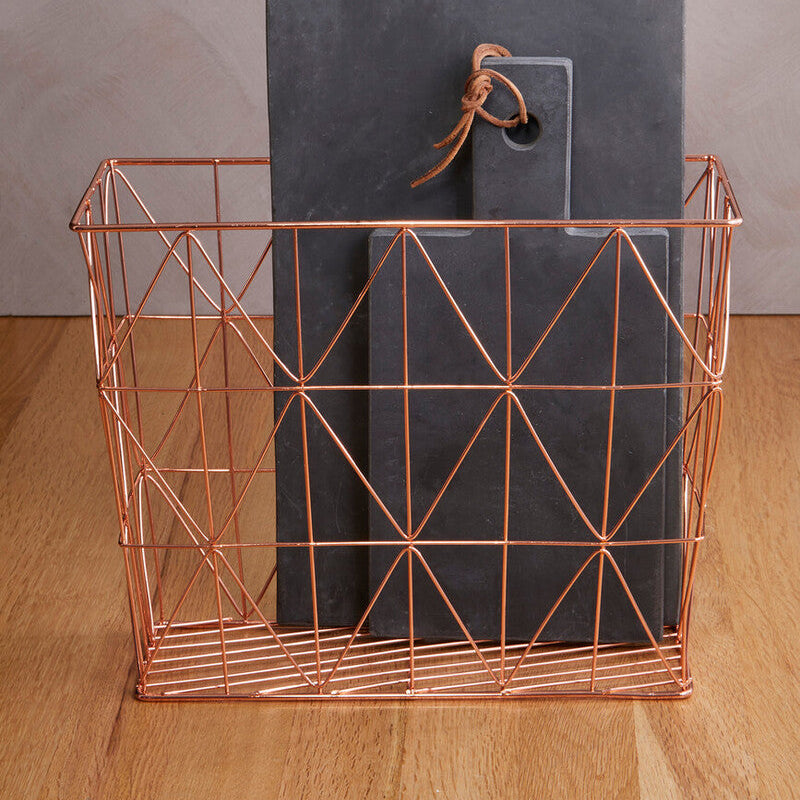 Copper wire basket with dark gray cutting boards on a wooden surface