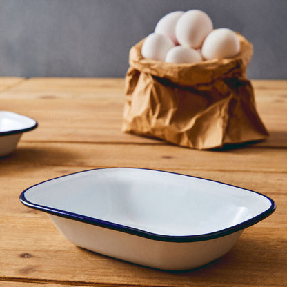 White enameled rectangular dish with blue rim on a wooden surface, with eggs in a brown paper bag in the background.