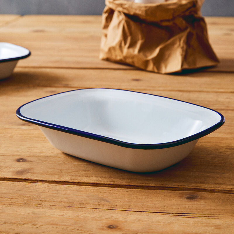 White enameled rectangular baking dish with blue rim on a wooden surface, eggs in a brown paper bag in the background.