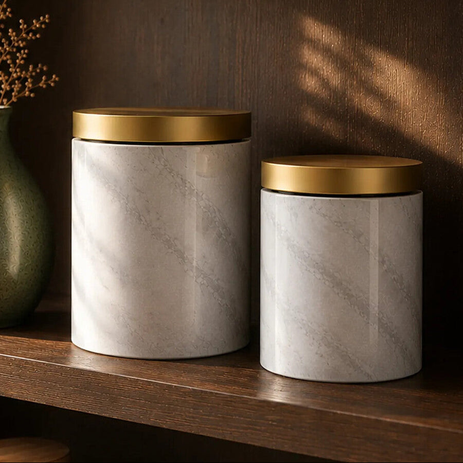 Two marble canisters with gold lids on a wooden shelf, labeled &