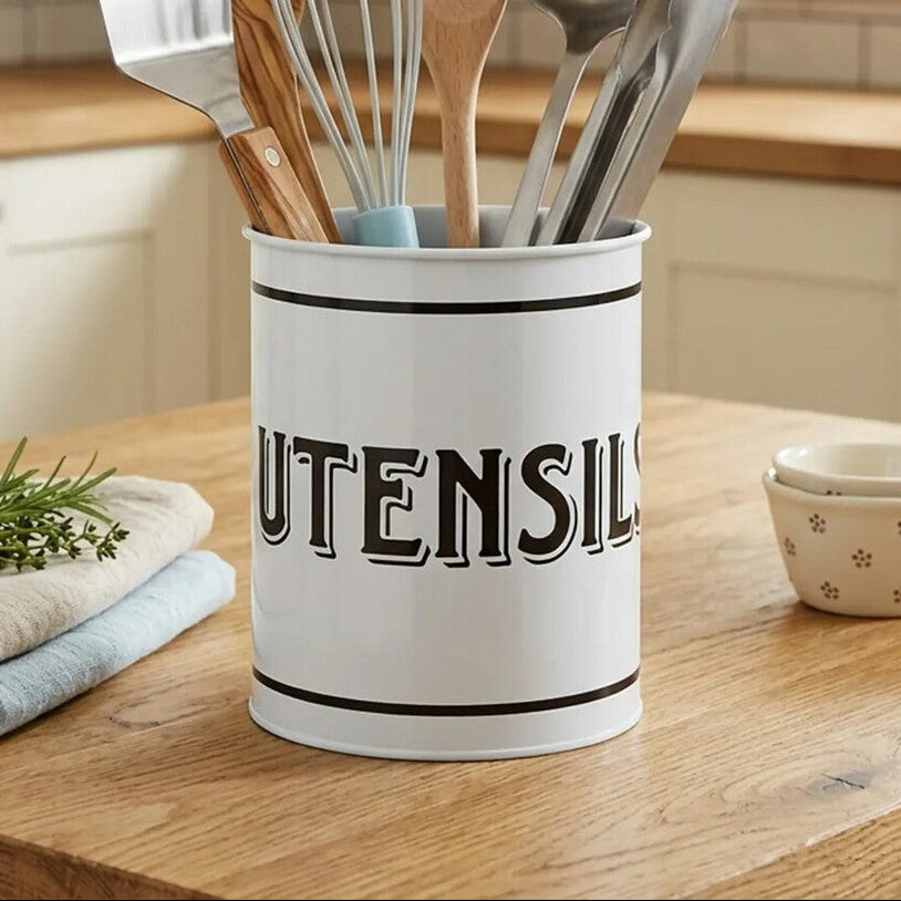 White utensil holder with kitchen utensils on a wooden countertop in a kitchen.