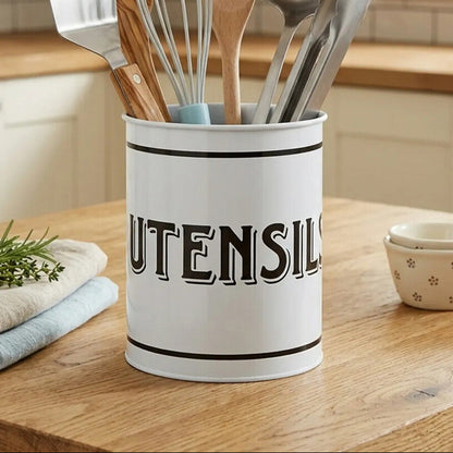 White utensil holder with kitchen utensils on a wooden countertop in a kitchen.
