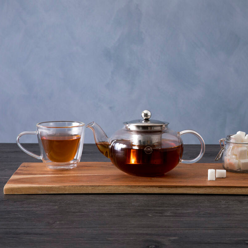 Tea set with teapot, glass cup, and sugar bowl on a wooden board against a gray background