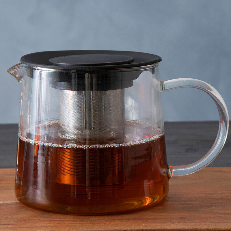 Clear glass teapot with black lid and handle on a wooden surface against a gray background