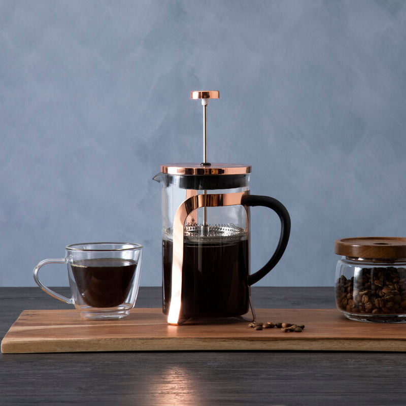 French press, glass of coffee, jar of coffee beans on a wooden board with a gray background