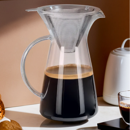 Coffee setup with a glass carafe, cup, and pastries on a reflective surface.