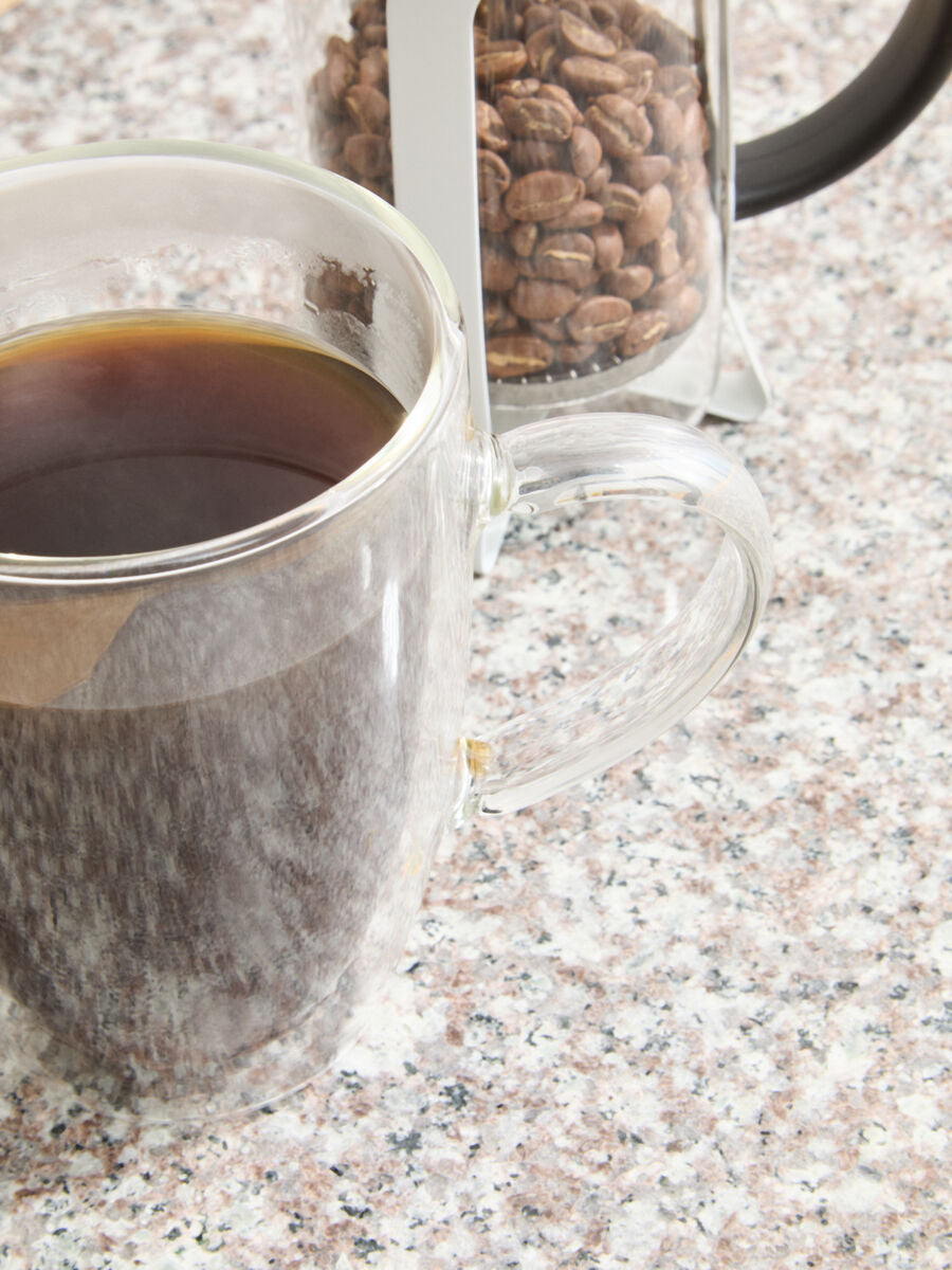 Clear glass mug with coffee and a container of coffee beans on a speckled countertop