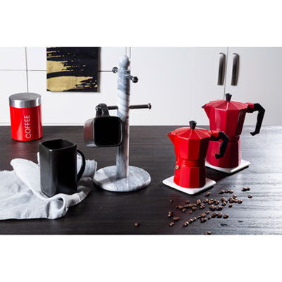 Red espresso pots and black mugs on a kitchen counter with coffee beans.