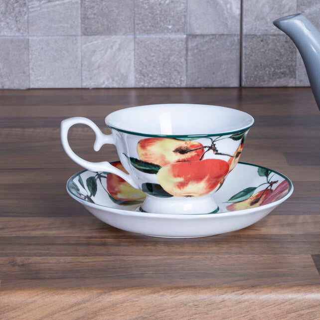 Teacup with fruit design on a saucer on a wooden surface with a tiled wall background