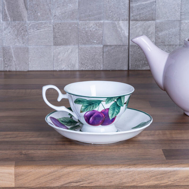 Teacup with floral design on a saucer next to a teapot on a wooden surface with a tiled wall background.