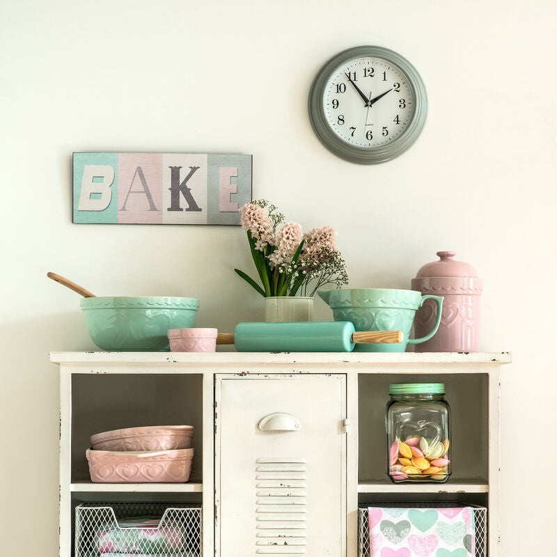 Kitchen cabinet with pastel-colored dishes and decor, including a clock on the wall.