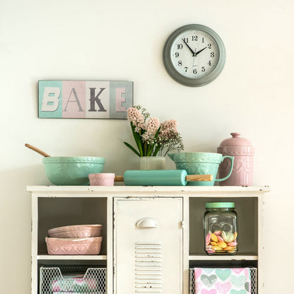 Kitchen cabinet with pastel-colored dishes and decor, including a clock on the wall.