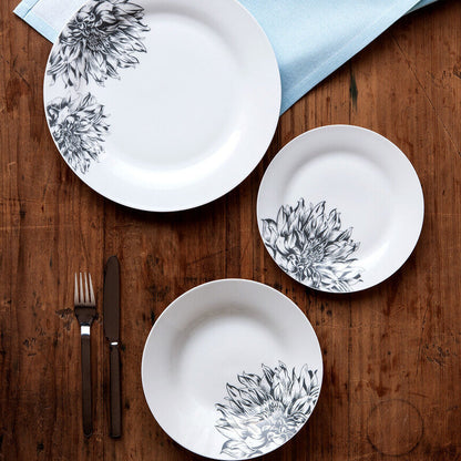 Set of white plates with black floral patterns on a wooden table with silverware.