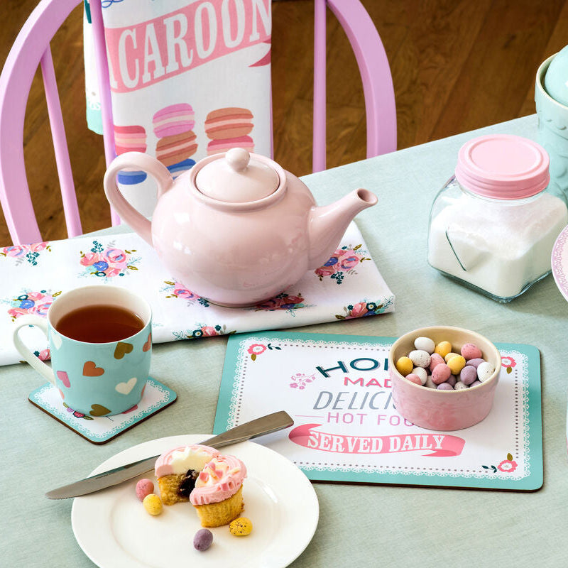 Tea set with teapot, cups, and cupcakes on a table.